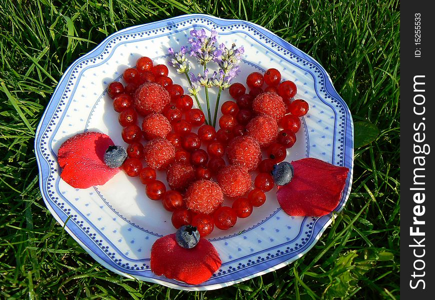 Red fruits heart on the plate with lavender and rose flower leaf. Red fruits heart on the plate with lavender and rose flower leaf