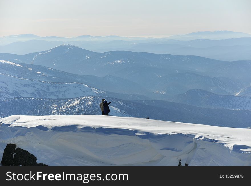 Two mountaineers on the edge over smoky blue hills, with snow cornice on foreground.