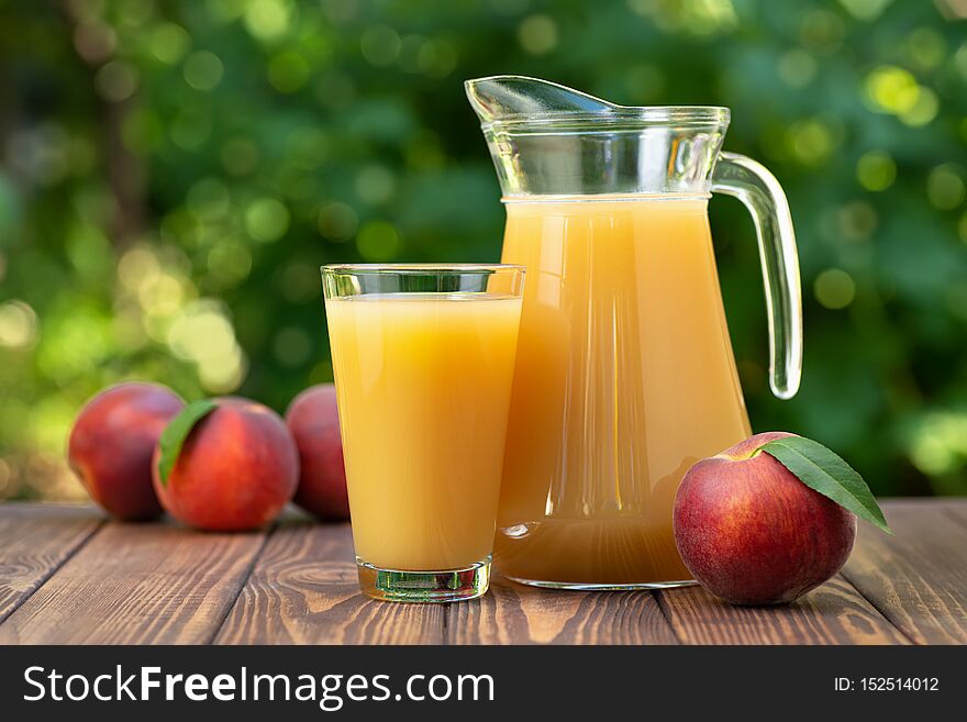 Peach juice in glass and jug with ripe fruits on wooden table outdoors. Summer refreshing drink