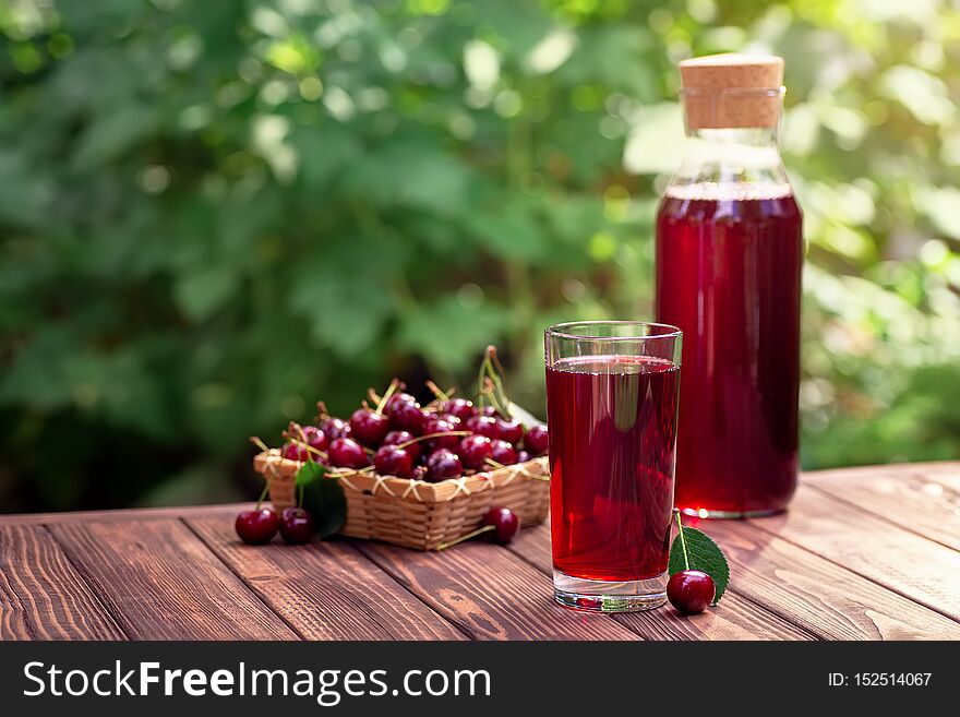 Cherry juice in glass and bottle with ripe berries on wooden table outdoors. Summer refreshing drink