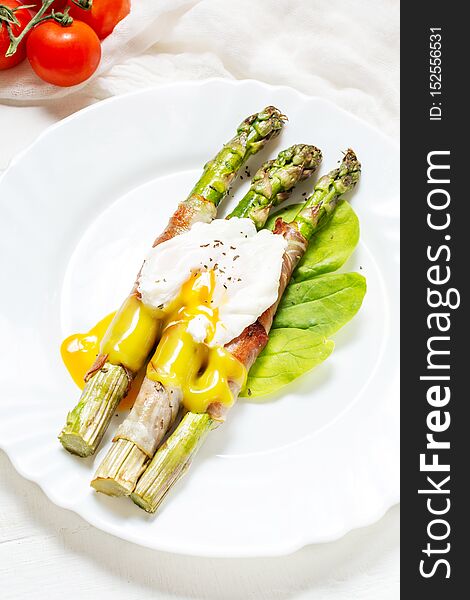 Grilled green asparagus wrapped with bacon, benedict poached egg on white wood background. Breakfast