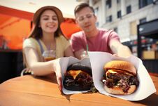 Young Happy Couple With Burgers In Street Cafe Royalty Free Stock Images
