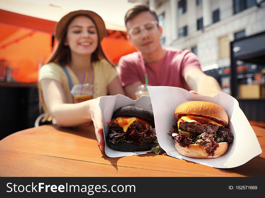 Young happy couple with burgers in street cafe, closeup