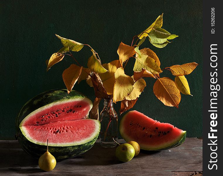 On a table cost yellow leaves in a glass bottle, alongside pears and cut water-melon lie on a table. On a table cost yellow leaves in a glass bottle, alongside pears and cut water-melon lie on a table.