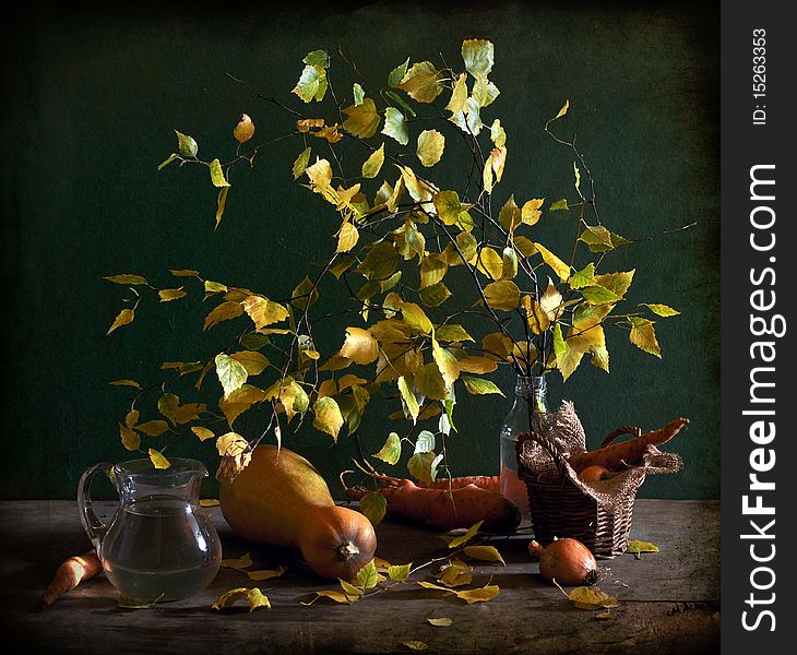 The yellow leaves of birch stand in a glass vase, a pumpkin and carrot lie alongside. The yellow leaves of birch stand in a glass vase, a pumpkin and carrot lie alongside.