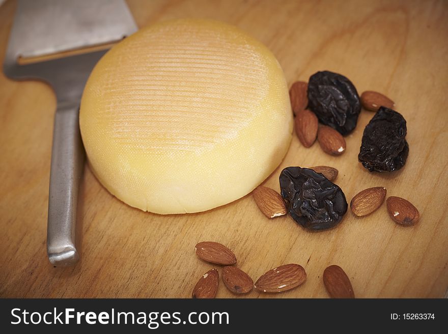 Cheese round with almonds and prunes on a wooden board.