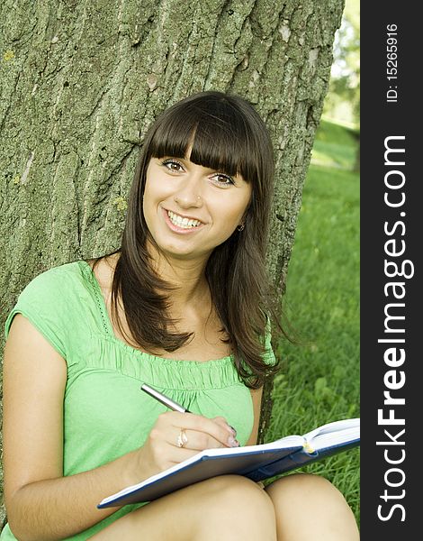 Young beautiful woman in a park with a notebook and pen. Thought of writing. Young beautiful woman in a park with a notebook and pen. Thought of writing