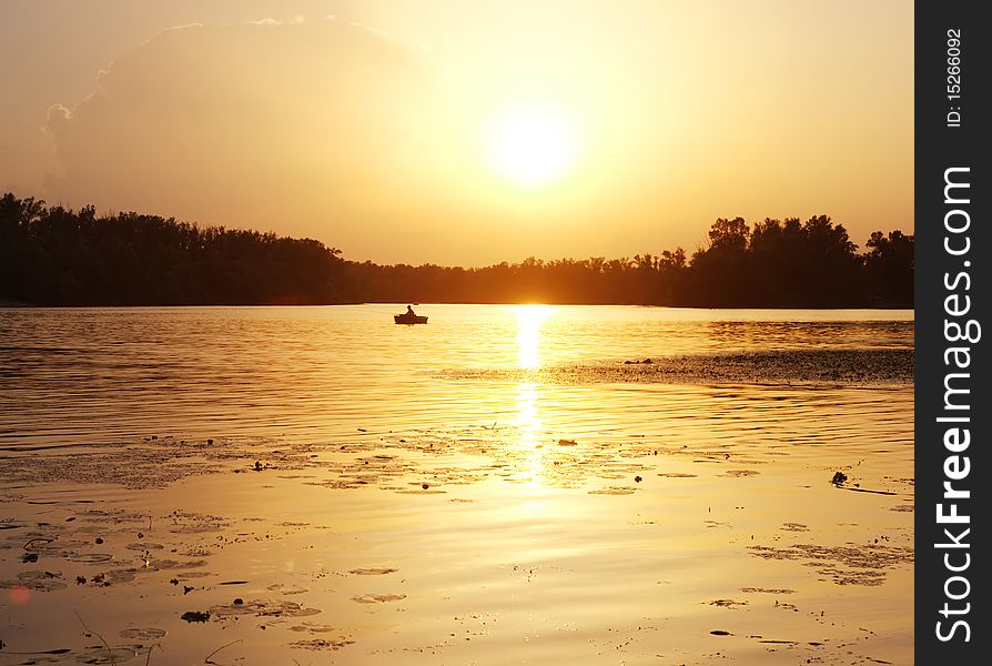 Silhouette of a fisherman on the river at sunset