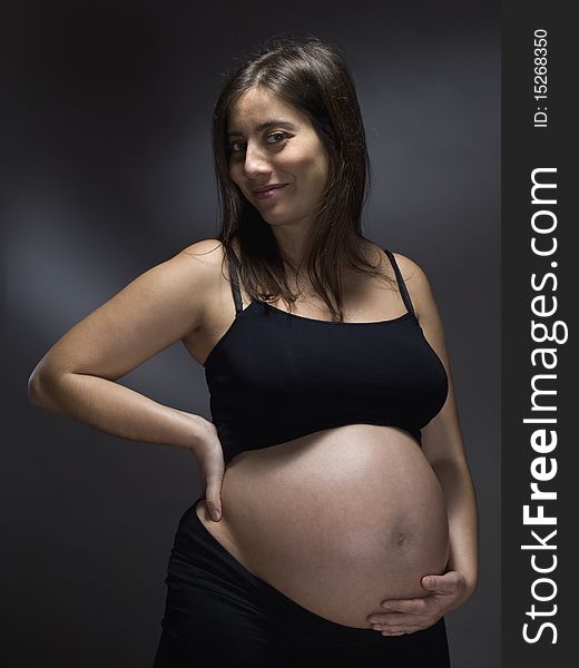 Pregnant woman holding her belly over a gray background.