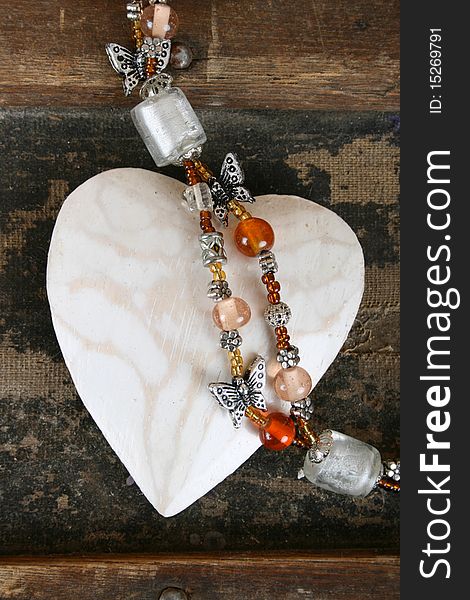 Carved wooden heart and beaded necklace on a wooden surface. Carved wooden heart and beaded necklace on a wooden surface