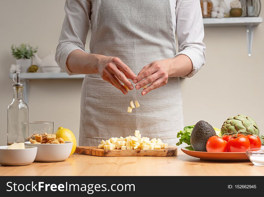 Cooking. A chef pours mozzarella or feta cheese, in the process of a vegetarian salad in the home kitchen. Light background.