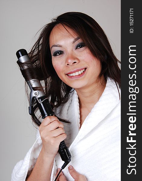 A pretty Chinese woman, is curling her hair, dressed in a white bath robe
for light gray background. A pretty Chinese woman, is curling her hair, dressed in a white bath robe
for light gray background.