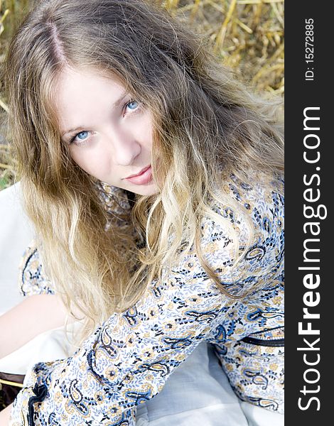 The woman with blue eyes and light hair sits on straw. The woman with blue eyes and light hair sits on straw