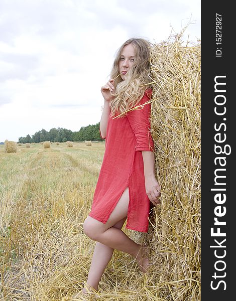 The woman in a red dress costs near a stack of straw and holds in a mouth a straw. The woman in a red dress costs near a stack of straw and holds in a mouth a straw