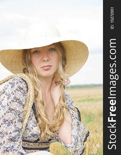 The girl with uncombed hair in a hat sits in the summer in the field of. The girl with uncombed hair in a hat sits in the summer in the field of