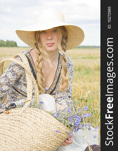 The woman in a hat sits in the summer in the field of with a basket of cornflowers. The woman in a hat sits in the summer in the field of with a basket of cornflowers
