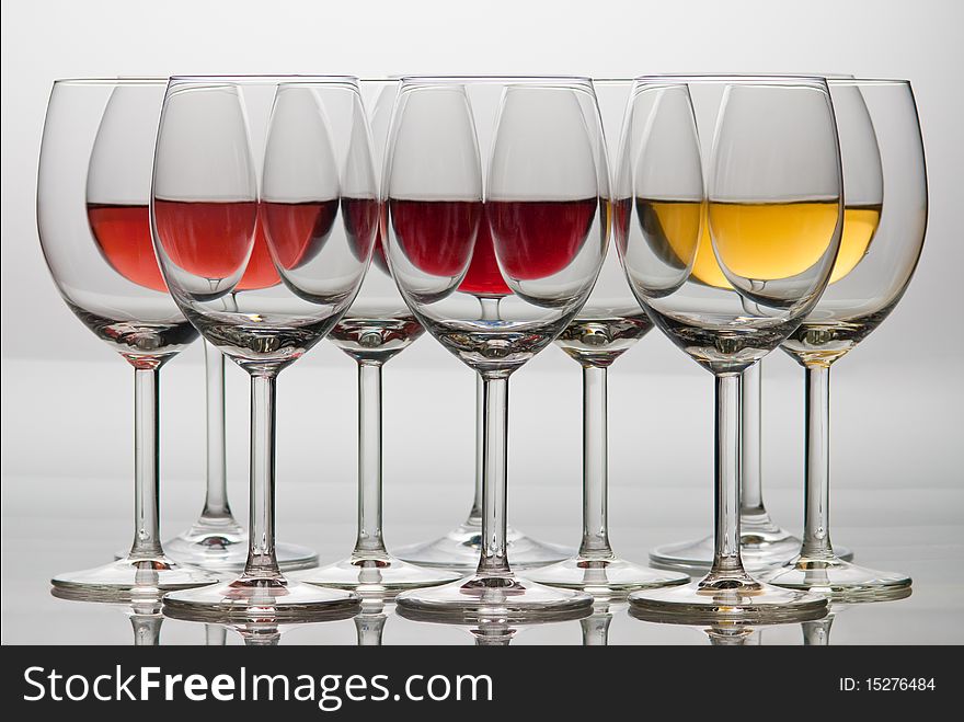 Ten wine glasses on reflex surface with mirroring. Three of them are with red, white and pink wine.