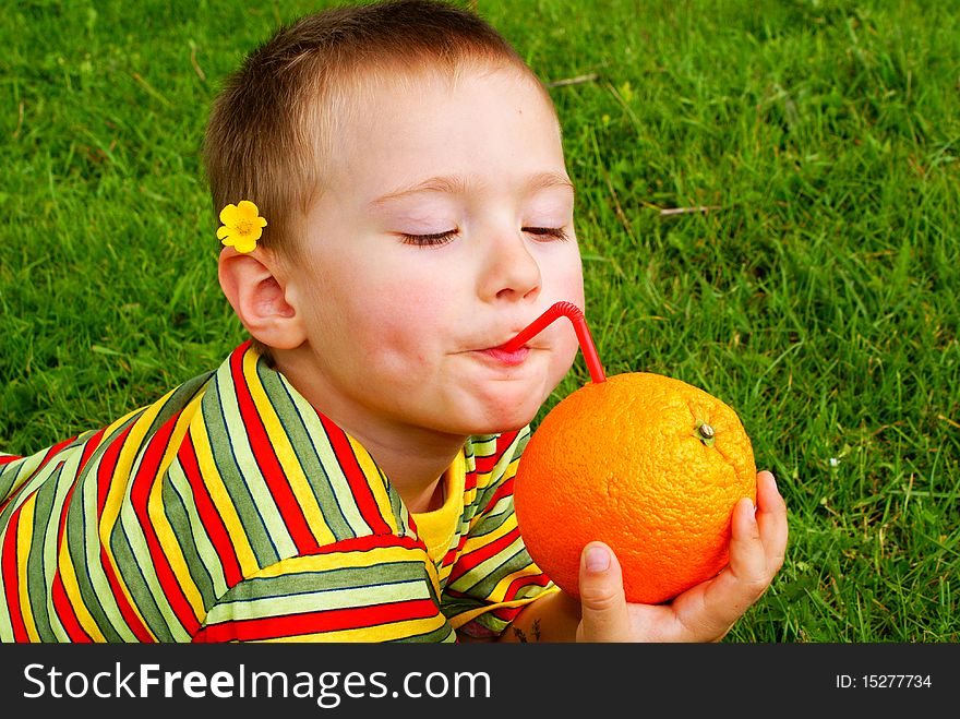 The child is drinking orange juice through a tube inserted in an orange background grass