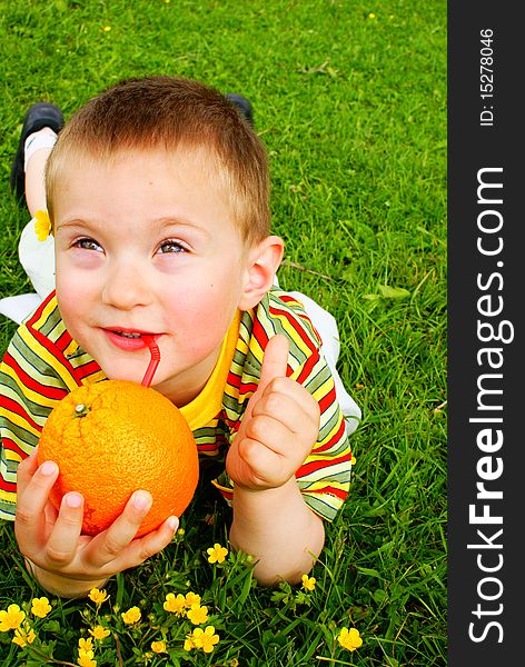 The child is drinking orange juice through a tube inserted in an orange background grass