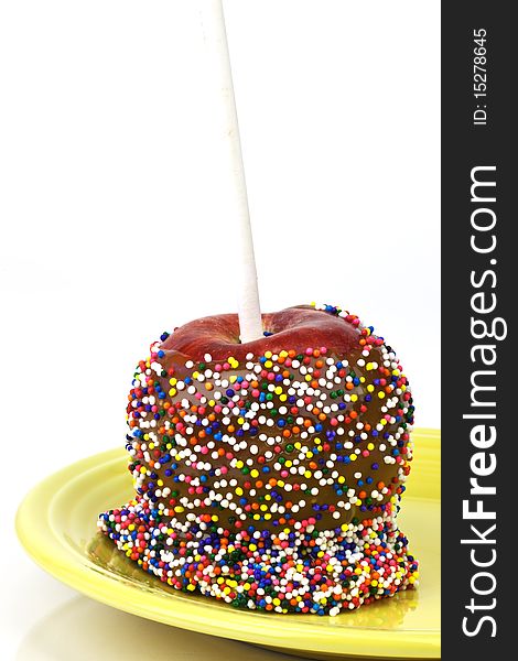 Closeup of caramel apple with rainbow sprinkles on a yellow plate over an isolated white background