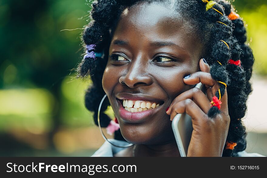 Portrait Of An African Beauty Smiling Young Black Woman In The Park With A Solar Flare Talking On The Phone