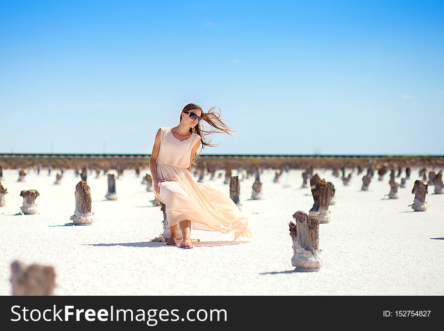 The girl in a white dress with the developing hair sits on a column on the salt lake.