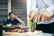 Asian Friends Are Using A Knife And A Fork To Cut The Grilled Meat On The Chopping Board To Bring Food Together With Friends Stock Images