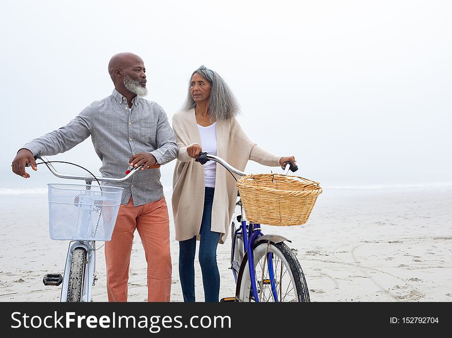 Front view of happy senior African-American couple standing with bicycles on the beach on cloudy day. Authentic Senior Retired Life Concept. Front view of happy senior African-American couple standing with bicycles on the beach on cloudy day. Authentic Senior Retired Life Concept