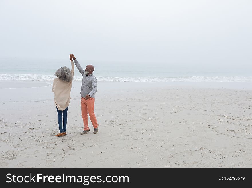 Front view of happy senior diverse couple dancing on the beach on cloudy day. Authentic Senior Retired Life Concept. Front view of happy senior diverse couple dancing on the beach on cloudy day. Authentic Senior Retired Life Concept