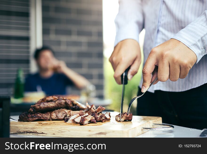 Asian friends are using a knife and a fork to cut the grilled meat on the chopping board to bring food together with friends