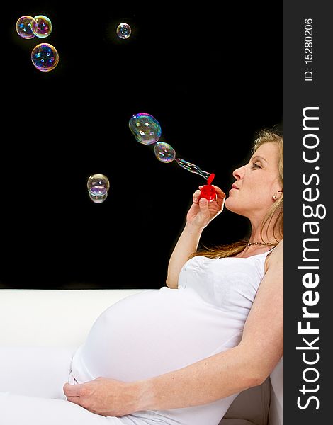 Young fresh pregnant woman with blow bubbles  sitting on a couch over black background. Young fresh pregnant woman with blow bubbles  sitting on a couch over black background.
