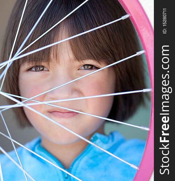 A young girl behind the spokes of a bike wheel. A young girl behind the spokes of a bike wheel.