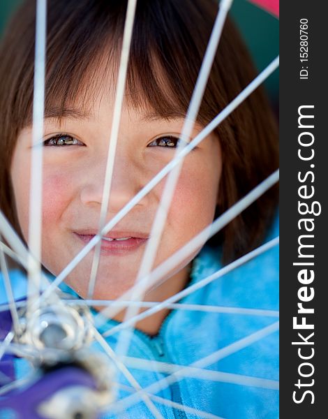 A young girl behind the spokes of a bike wheel. A young girl behind the spokes of a bike wheel.