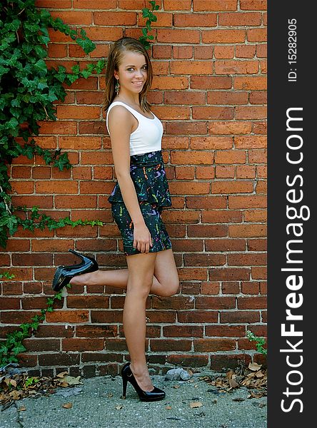 Beautiful teen girl standing casually against a brick wall on a warm summer day.