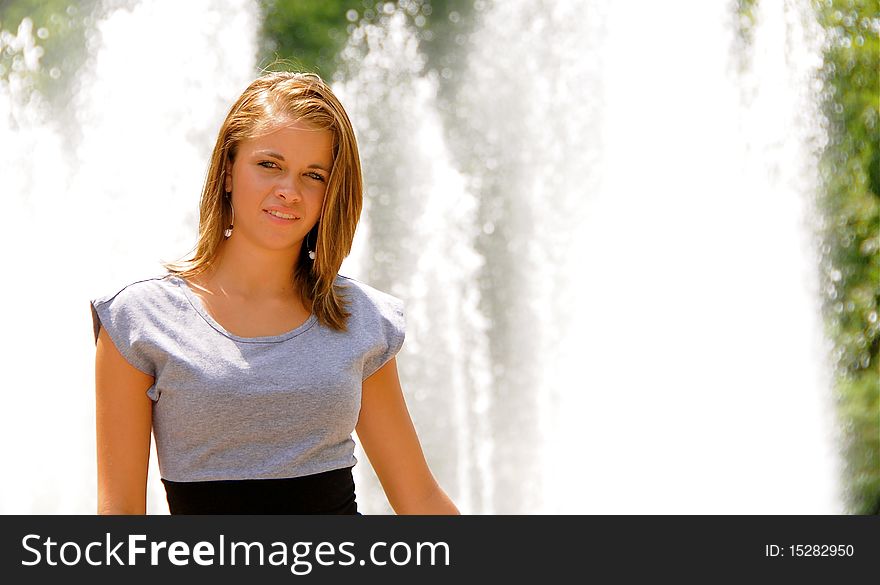 Beautiful teen girl posing for photographs in front of a fountain on a hot summer day.