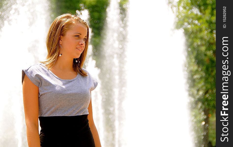Attractive teen girl in front of a fountain on a hot summer day.