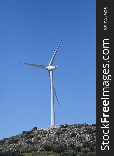 A Wind Turbine on a hilltop with clear blue sky.