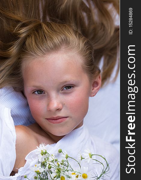 The young girl with light hair in a white shirt with camomiles smiles. The young girl with light hair in a white shirt with camomiles smiles