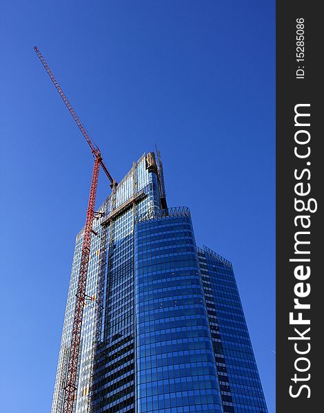 Modern building and hoist crane on the background of the blue sky. Modern building and hoist crane on the background of the blue sky