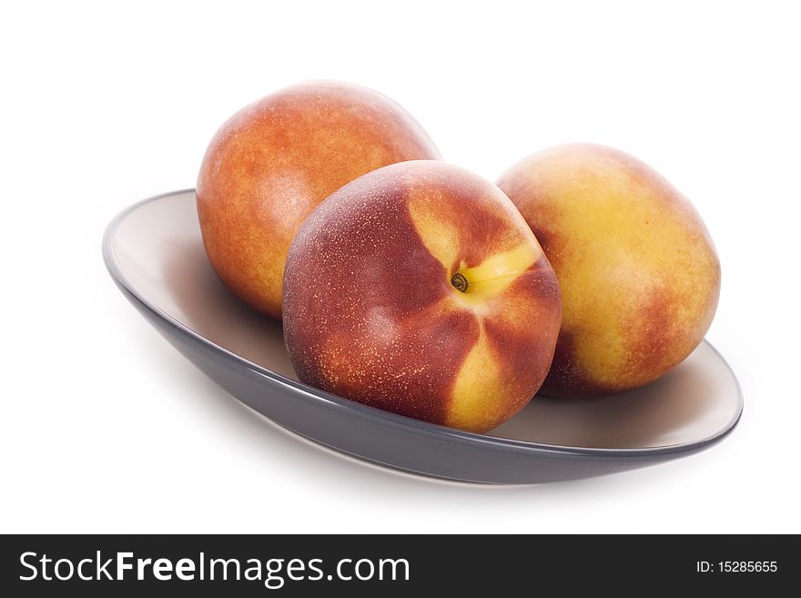 Three peaches lie on a plate. Isolated white background
