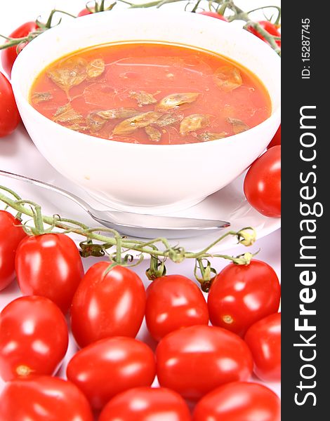 Tomato soup with basil leaves with fresh tomatoes around it and a spoon