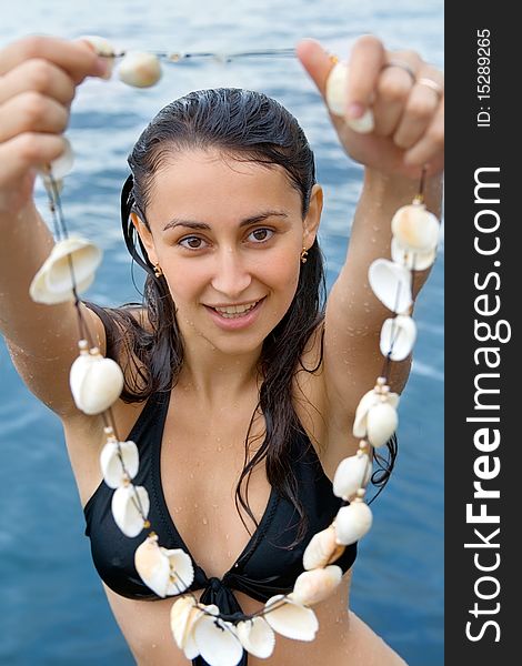Pretty girl holding beads made of seashells, standing near the sea. Pretty girl holding beads made of seashells, standing near the sea