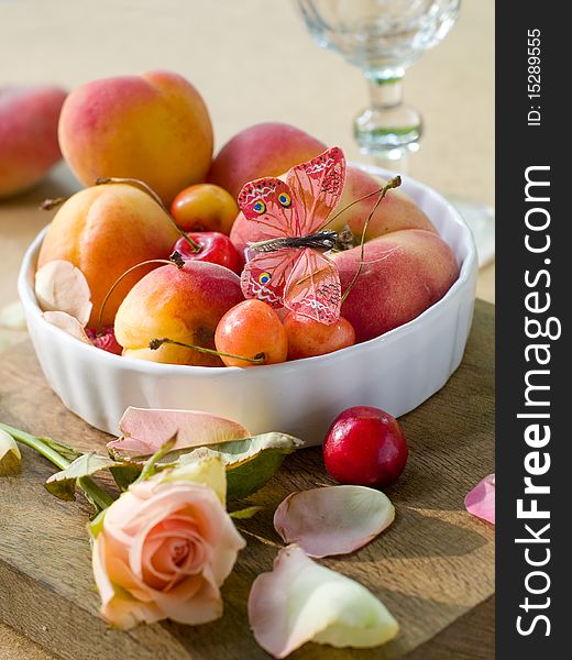 Fresh apricots, plums, cherry in bowl with butterfly rose on foreground. Fresh apricots, plums, cherry in bowl with butterfly rose on foreground