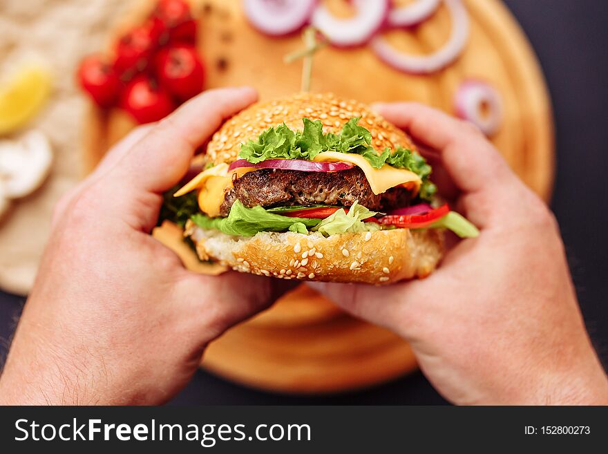 Hands holding fresh delicious burger with french fries, sauce on the wooden table top view. Horizontal view copy space
