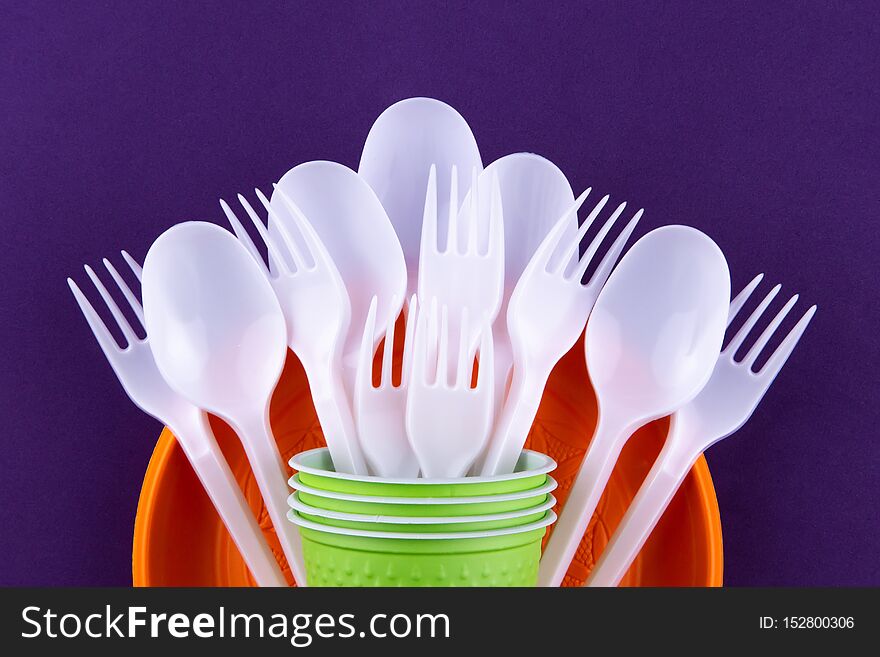 Bright orange and green set of disposable plastic tableware on purple background. Ecology problem. No plastic concept