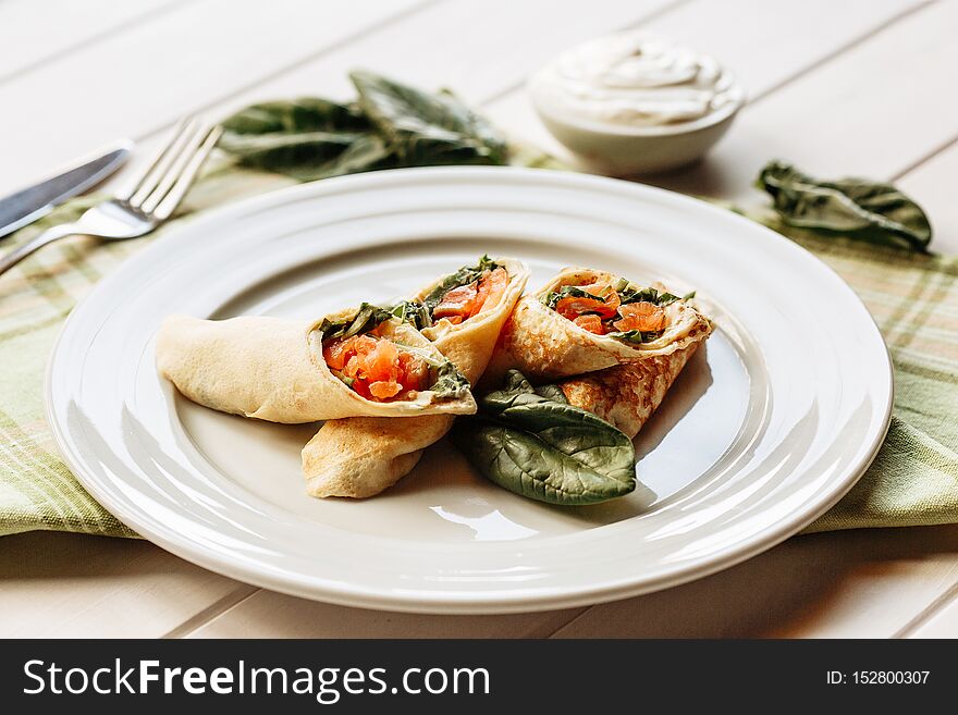 Rolls of thin pancakes with smoked salmon, horseradish cream cheese and spinach leaves. Side view with copy space.