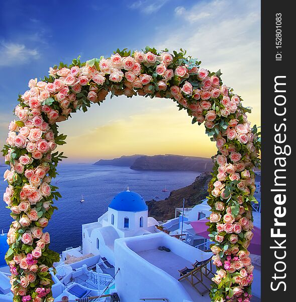 Wedding at Santorini. Beautiful arch decorated with flowers of roses with  blue church of Oia, Santorini, Greece at most romantic