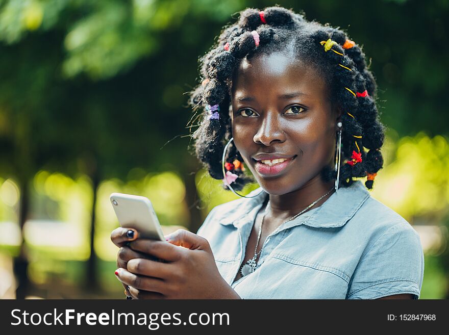 Portrait of African beauty smiling young black woman in the park with a solar flare writing a message in the phone