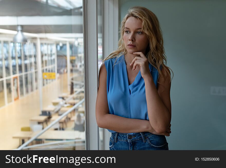 Front view of thoughtful Caucasian businesswoman looking through window in office. This is a casual creative start-up business office for a diverse team