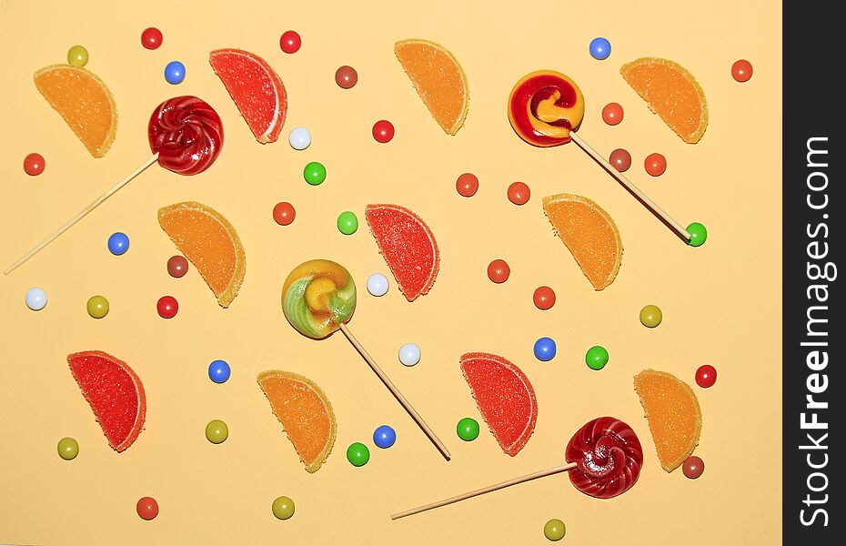 Multicolored dragee, lollipops and marmalade slices of lemon on a yellow background